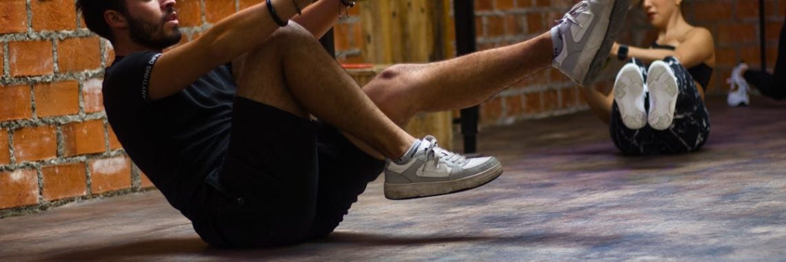 A man and woman perform core exercises with a medicine ball in a brick wall gym.