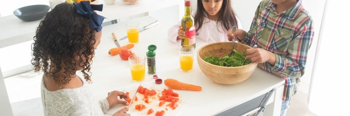 Three children preparing a fresh vegetable salad together in a bright kitchen.
