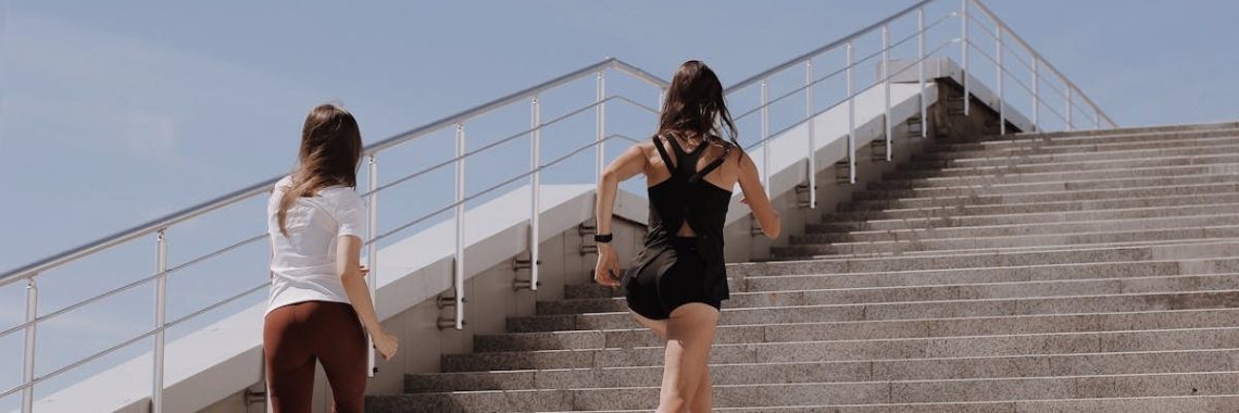 Two women running up stairs outdoors, embodying fitness and wellness.